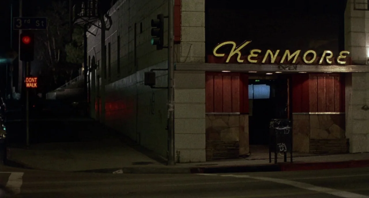 Barfly (1987) movie still: establishing — A street corner at night features a building with a large illuminated neon sign. A red traffic light and a…
