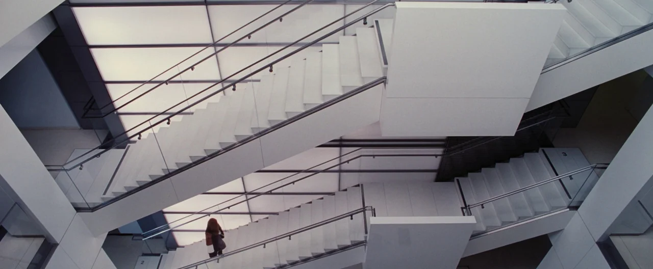 Nocturnal Animals (2016) movie still: wide — A modern building interior features a minimalist white staircase with glass railings. A lone woman…
