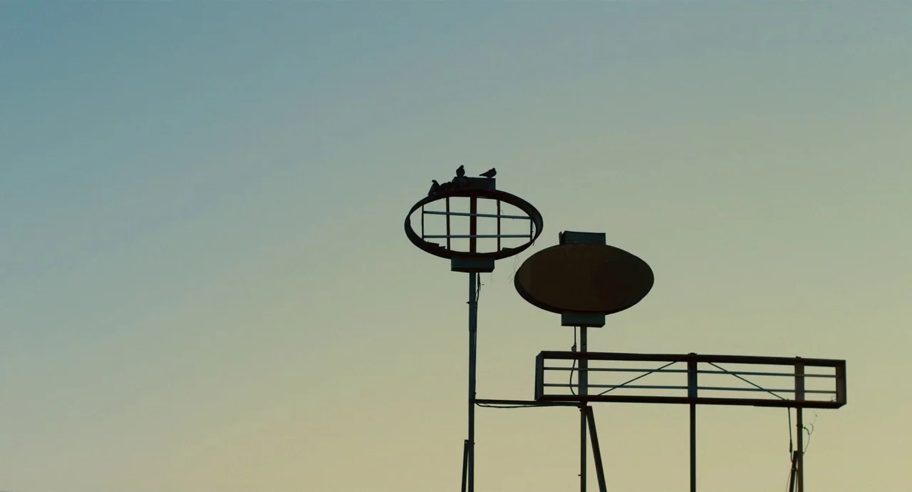 Palo Alto (2013) movie still: establishing — A tall metal structure stands against a clear, pale sky at twilight. Several small birds rest on top of…