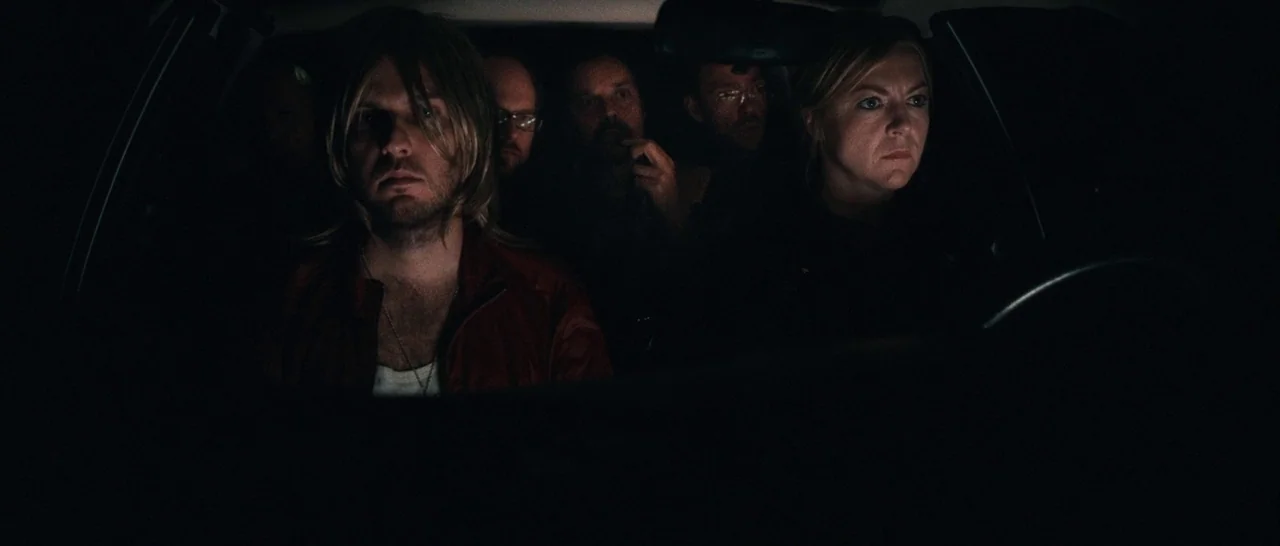 Sound of Noise (2010) movie still: medium — The interior of a car is dimly lit at night. Multiple people sit in the vehicle looking ahead in silence.