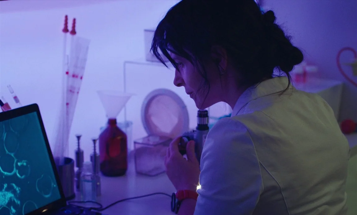 High Life (2018) movie still: medium — A dark laboratory workspace contains various glassware and a glowing computer monitor. A woman in a white…