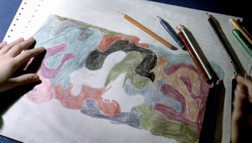 The Seventh Continent (1989) movie still: closeup — A sheet of white paper lies on a dark blue surface covered in drawings. The drawing consists of…