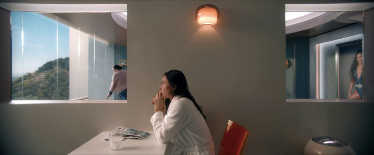 The Substance (2024) movie still: medium — A minimalist white room features a symmetrical design with two large framed windows. A woman in a white…