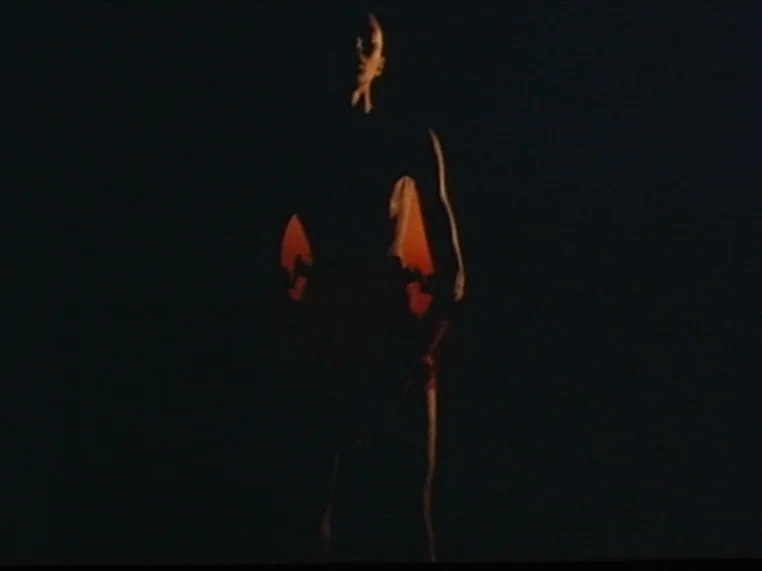 Salome (1972) movie still: fullbody — A person stands in a pitch black room with only thin lines of light. The subject is backlit with orange light…