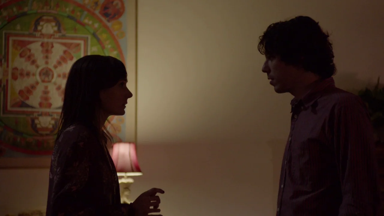 The Heart Machine (2014) movie still: medium — A dimly lit room features a colorful mandala artwork hanging on the wall. A man and a woman stand in…