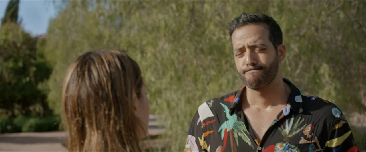 An Endless Wedding (2025) movie still: medium — An outdoor park setting with dense green trees visible in the soft-focus background. A bearded man…