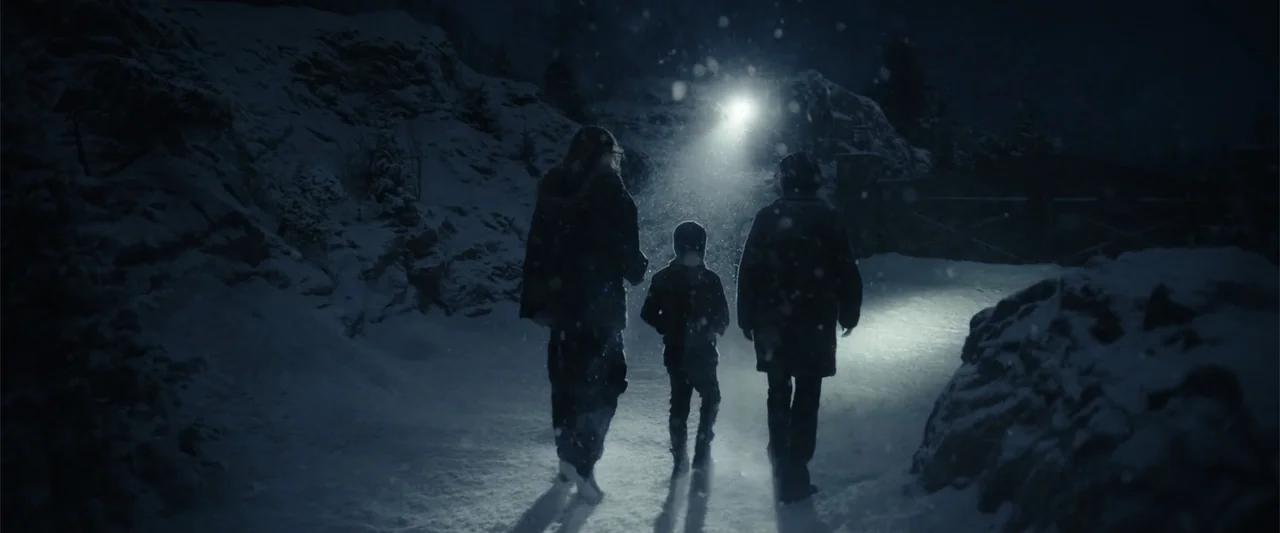 Moonfall (2022) movie still: fullbody — A dark, snow-covered road at night is lit by a single bright light source. Three people in heavy winter…