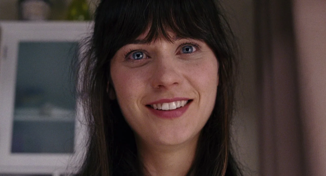 The Happening (2008) movie still: closeup — A woman stands in an indoor space with a white cabinet visible behind her. She smiles while looking…