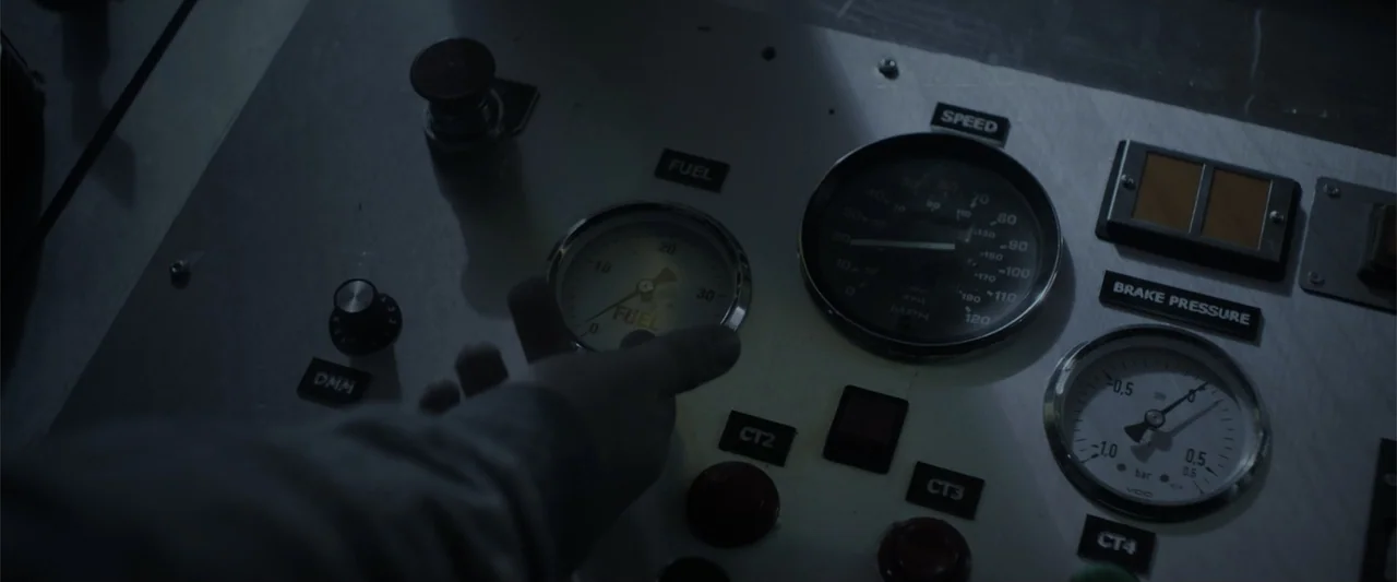 Howl (2015) movie still: closeup — A metal control panel features several analog gauges for fuel, speed, and brake pressure. A person's hand reaches…