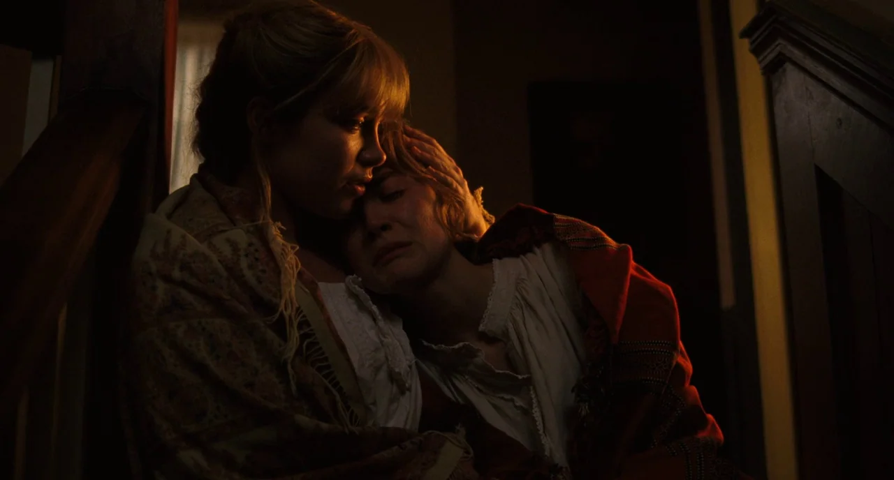 Little Women (2019) movie still: medium — A dimly lit wooden staircase features two women sitting in close proximity. One woman embraces the other…