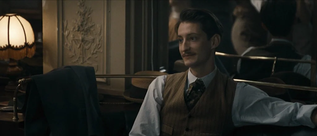 Frantz (2016) movie still: medium — A dimly lit 1930s establishment features ornate wall molding and vintage table lamps. A young man sits at a dark…