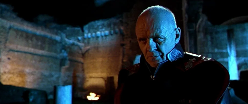 Titus (1999) movie still: medium — Ancient stone ruins are dimly lit at night with crumbling walls in the background. A man stands in the…
