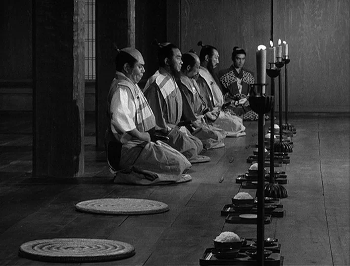 Throne of Blood (1957) movie still: medium — A dark wooden hall contains a line of samurai kneeling in traditional attire. Several tall candles in…