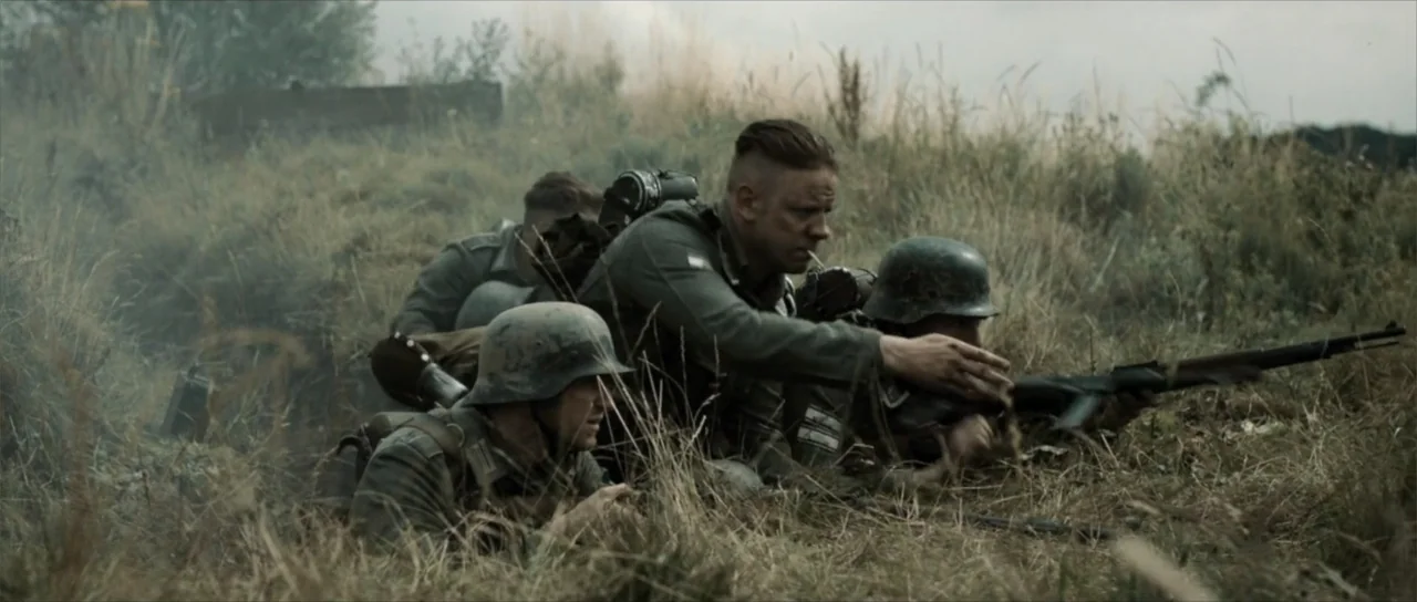 Sin retorno (2009) movie still: medium — A grassy trench area holds three soldiers positioned in the tall vegetation. The men wear field uniforms…