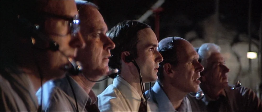 Close Encounters Of The Third Kind (1977) movie still: medium — Five men wearing headsets sit in a row inside a dark monitoring room. They all look…