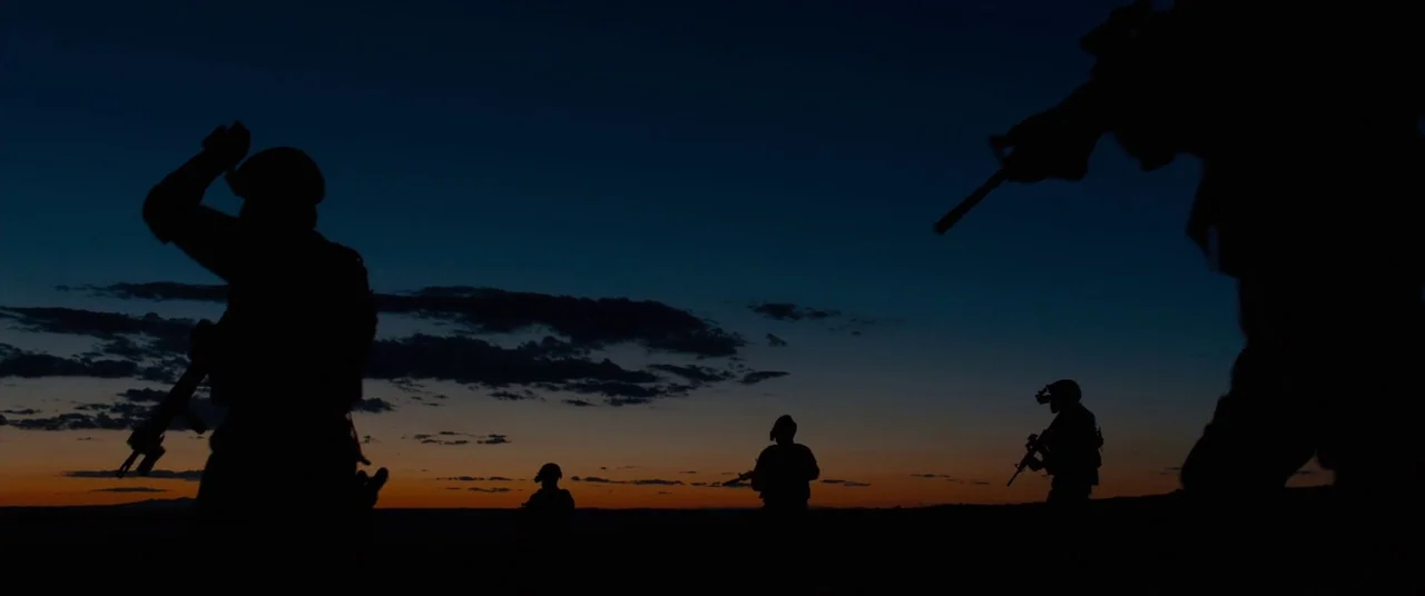 Sicario (2015) movie still: wide — A group of soldiers stands in the desert during the dim light of dusk. The dark silhouettes of the armed figures…