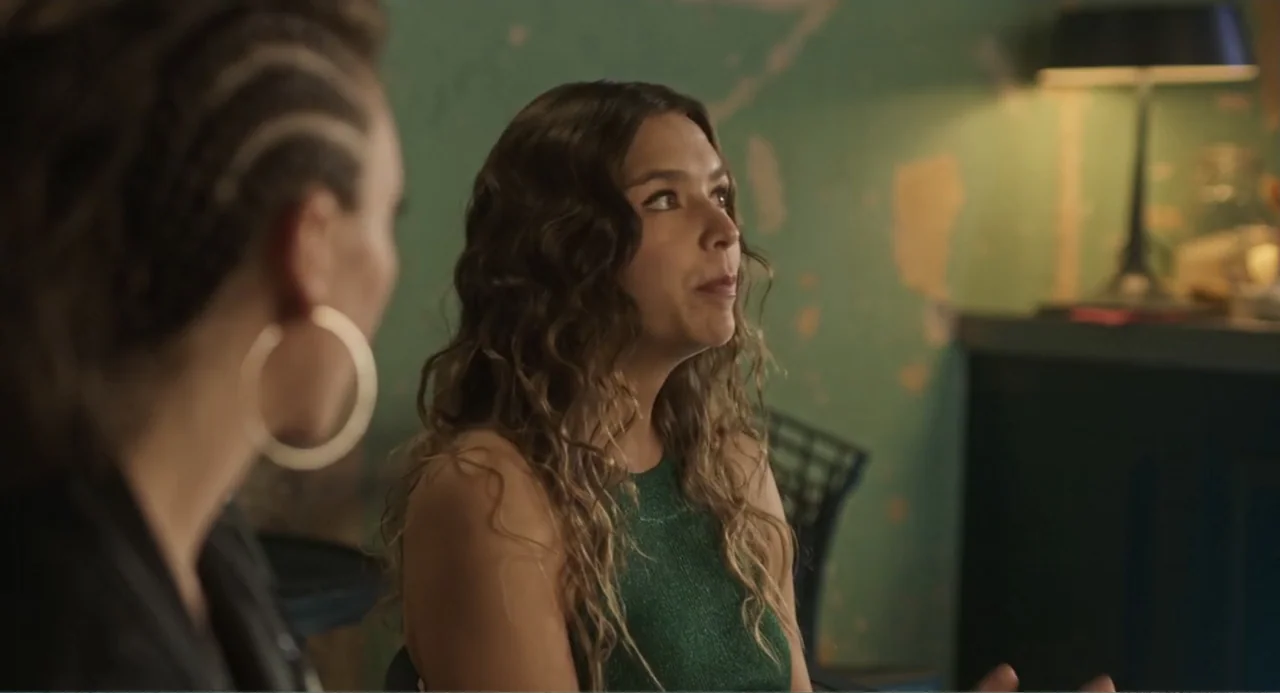 Casando a mi Ex (2023) movie still: medium — A dark indoor space features a teal painted wall with visible texture and wear. A woman with long wavy…