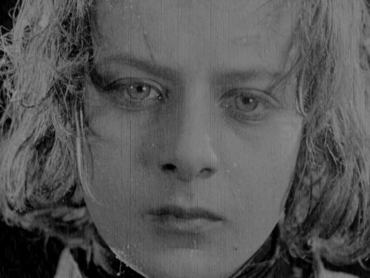 Napoleon (1927) movie still: closeup — A close portrait shot captures a young woman face against a dark, featureless backdrop. She maintains steady…