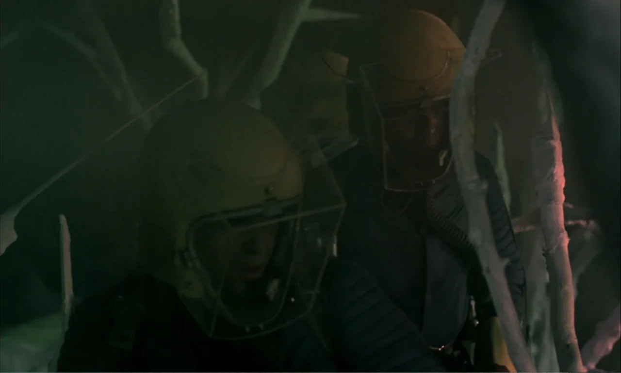Journey to the Seventh Planet (1962) movie still: medium — A dark environment populated by skeletal branches under low-key lighting. Two figures in…