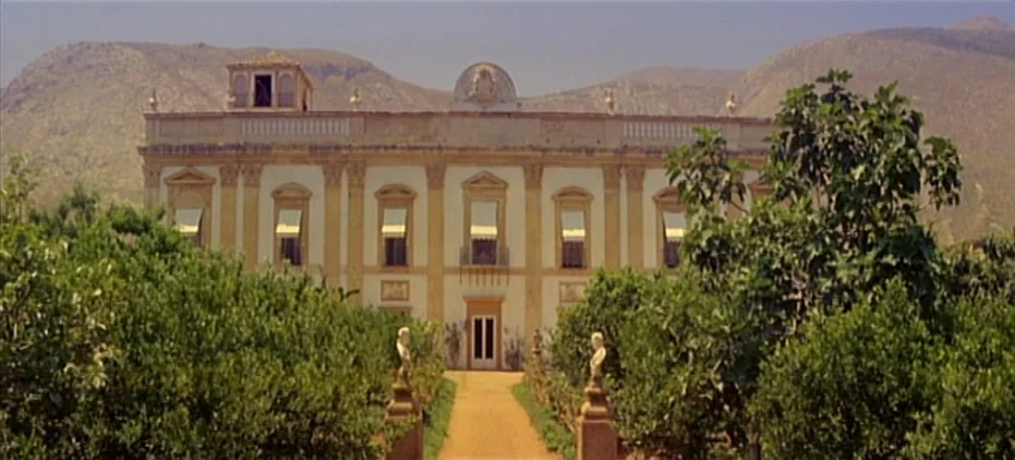 The Leopard (1963) movie still: establishing — A neoclassical villa features a symmetrical facade with cream walls and shuttered windows. A straight…