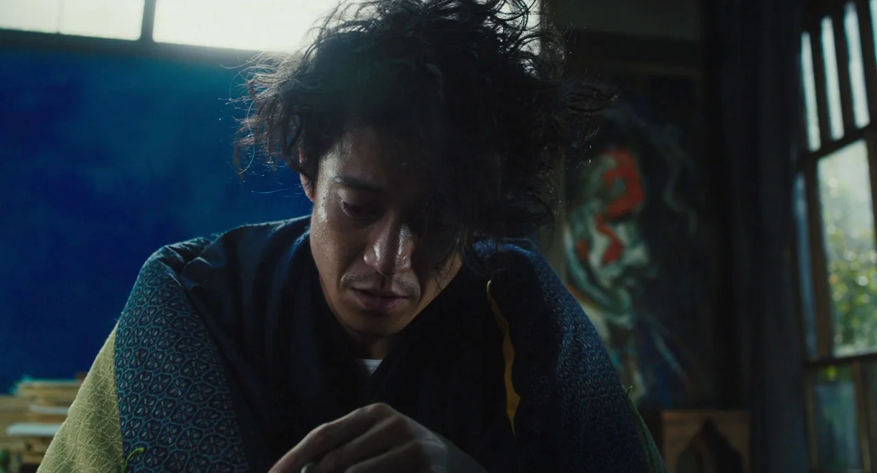 No Longer Human (2019) movie still: medium — An artist is positioned in a sunlit workspace featuring a large canvas. He leans forward while…