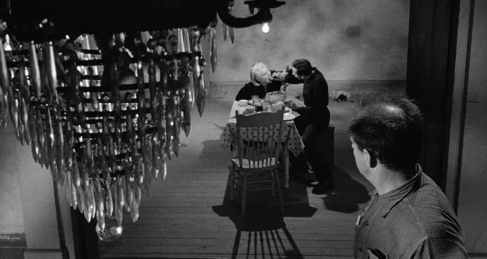 Baby Doll (1956) movie still: wide — A sparse room with a large, ornate crystal chandelier hanging low over a table. A man feeds an elderly woman…