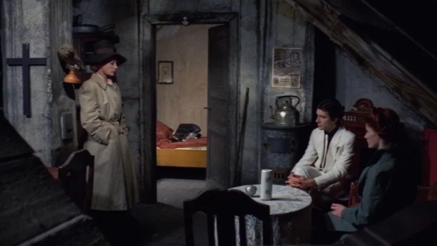 Tenderness of the Wolves (1973) movie still: medium — An attic room features rough, unpainted walls, exposed beams, and a dark wooden cross. Three…