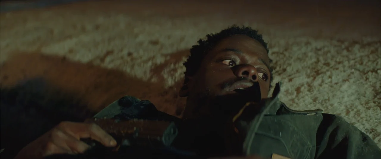 Queen & Slim (2019) movie still: closeup — A man lies in the dirt at night under low light. He clutches a handgun while looking off-screen.