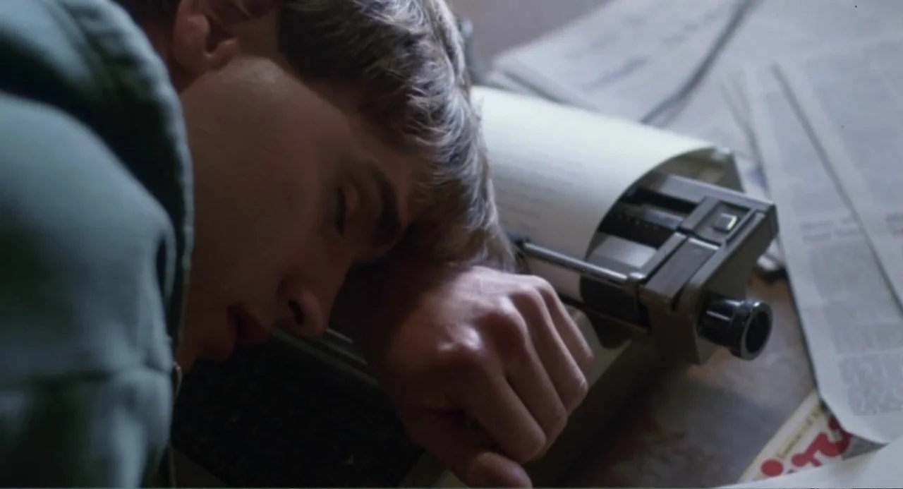 Dangerously Close (1986) movie still: closeup — A workspace features a vintage manual typewriter and scattered stacks of paper. A man lies face down…