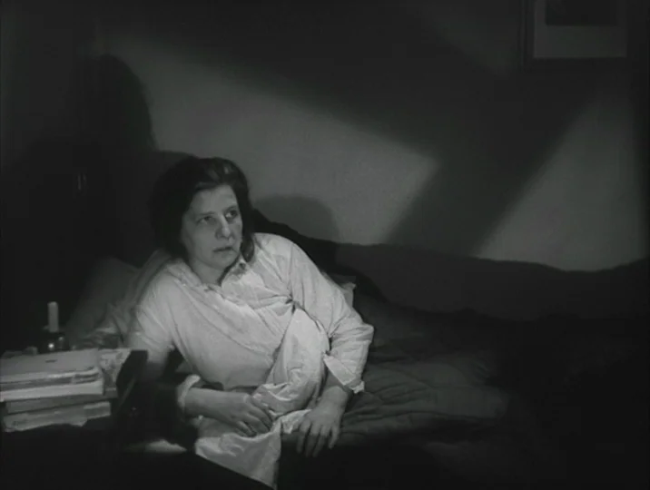 Crisis (1946) movie still: medium — A dimly lit room with a subject sitting up against pillows on a bed. The person looks slightly off-camera while…