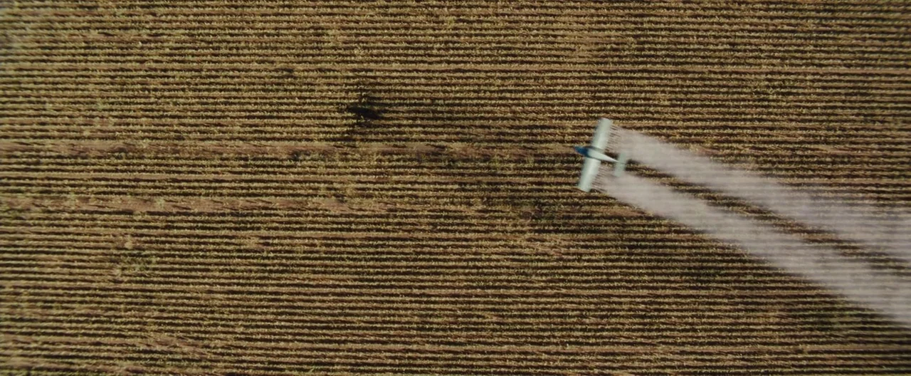 The Burning Plain (2008) movie still: establishing — A vast, brown, harvested crop field is viewed from directly overhead. A small agricultural…
