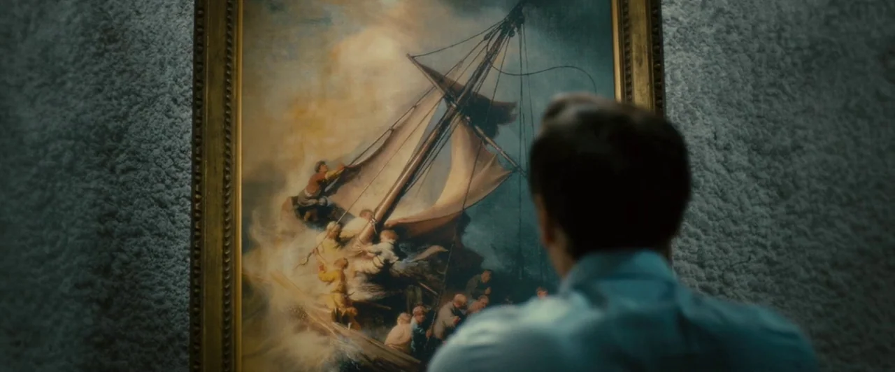 Trance (2013) movie still: medium — An interior space features a large gold-framed painting of a storm-tossed ship on a wall. A man in a blue shirt…