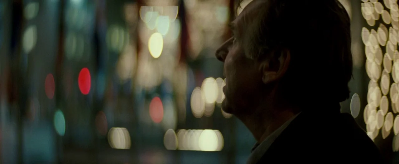 Michael Clayton (2007) movie still: closeup — A man stands at night in a city with heavy bokeh from distant lights. The man looks ahead into the…