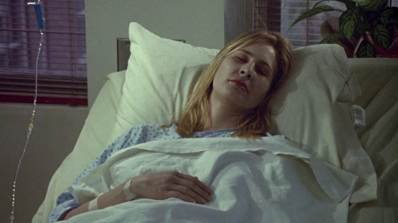 Bride of Reanimator (1989) movie still: medium — A hospital room with a patient lying in a bed against a window. A woman with blonde hair sleeps in…