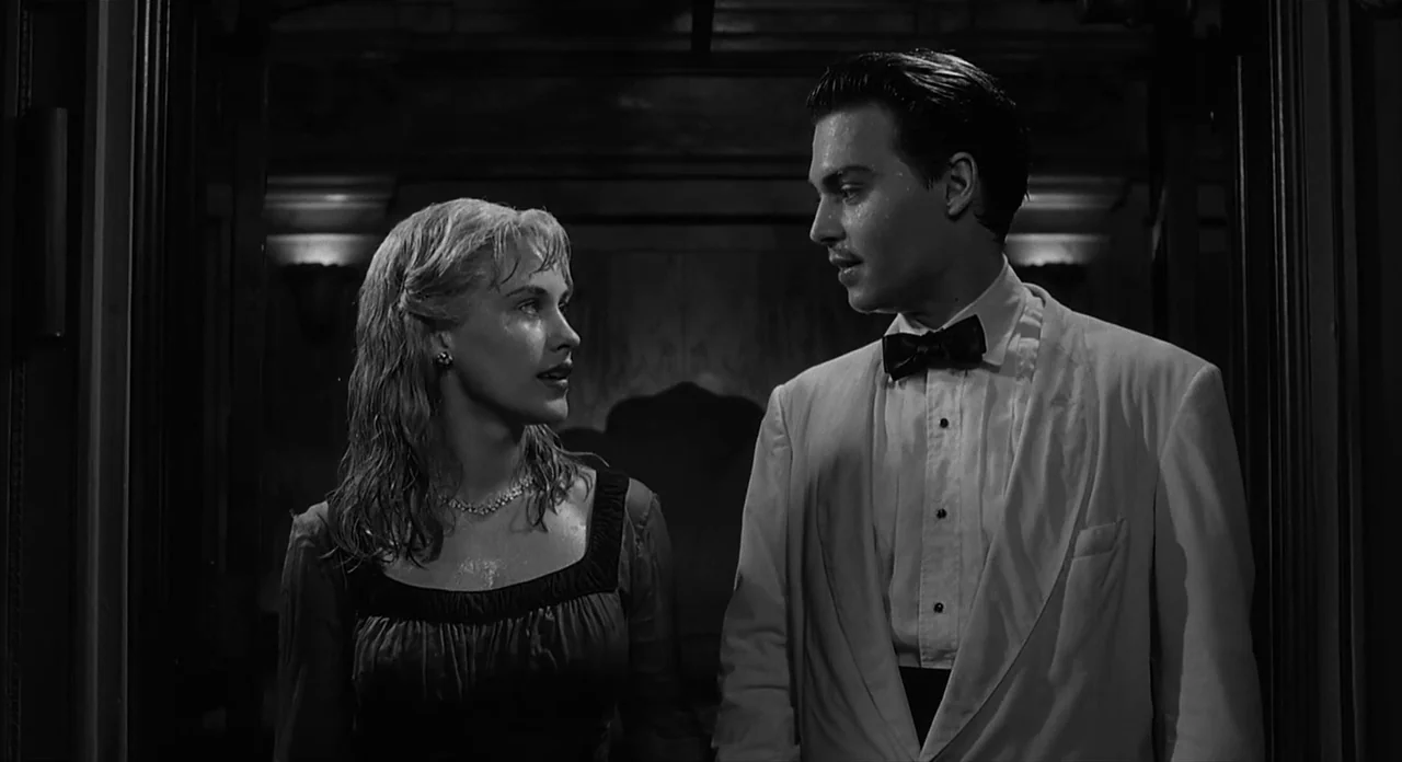 Ed Wood (1994) movie still: medium — A dimly lit indoor hallway with dark wood paneling and architectural molding. A young man in a tuxedo and a…