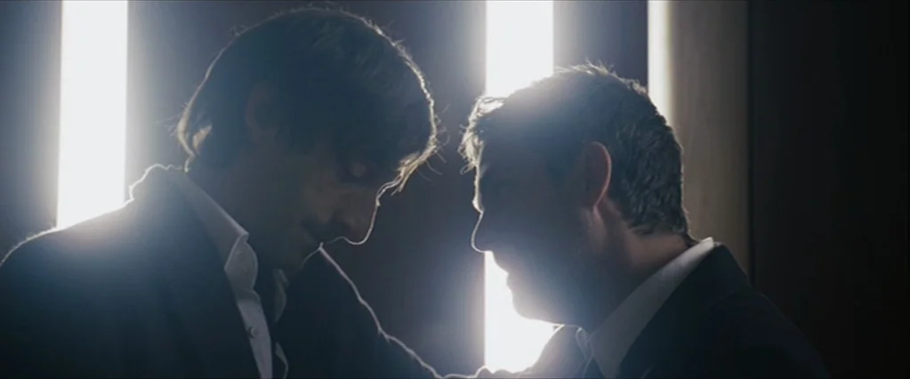 The Brothers Bloom (2008) movie still: medium — A dimly lit interior corridor features vertical light panels casting bright highlights on the…