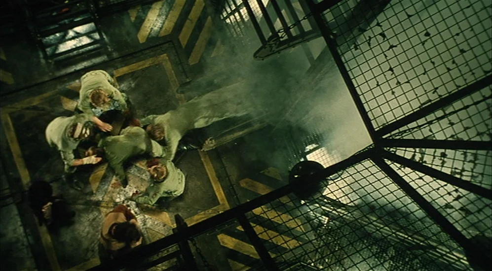 The City Of Lost Children movie still: wide — An industrial metal platform features yellow warning stripes and black wire mesh safety railings.…