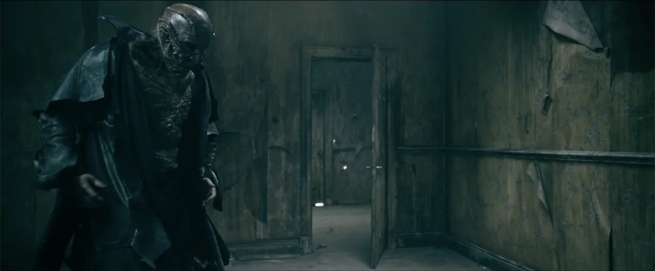 Jeepers Creepers: Reborn (2022) movie still: medium — A dark, dilapidated interior space features peeling wallpaper and a half-open wooden door. A…