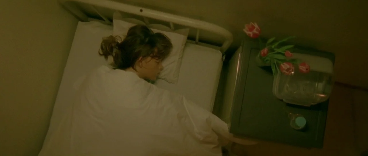 Enter The Void (2009) movie still: medium — A small hospital room features a metal bed frame and a dark side table. A woman lies asleep under a…