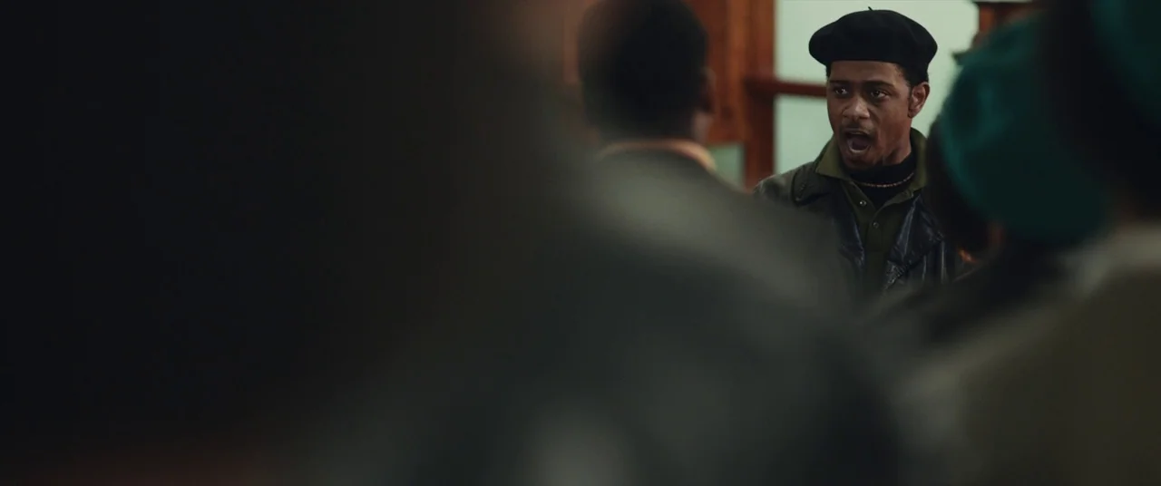 Judas and the Black Messiah (2021) movie still: medium — A crowded interior space with figures blurred in the foreground and blurred wood paneling.…