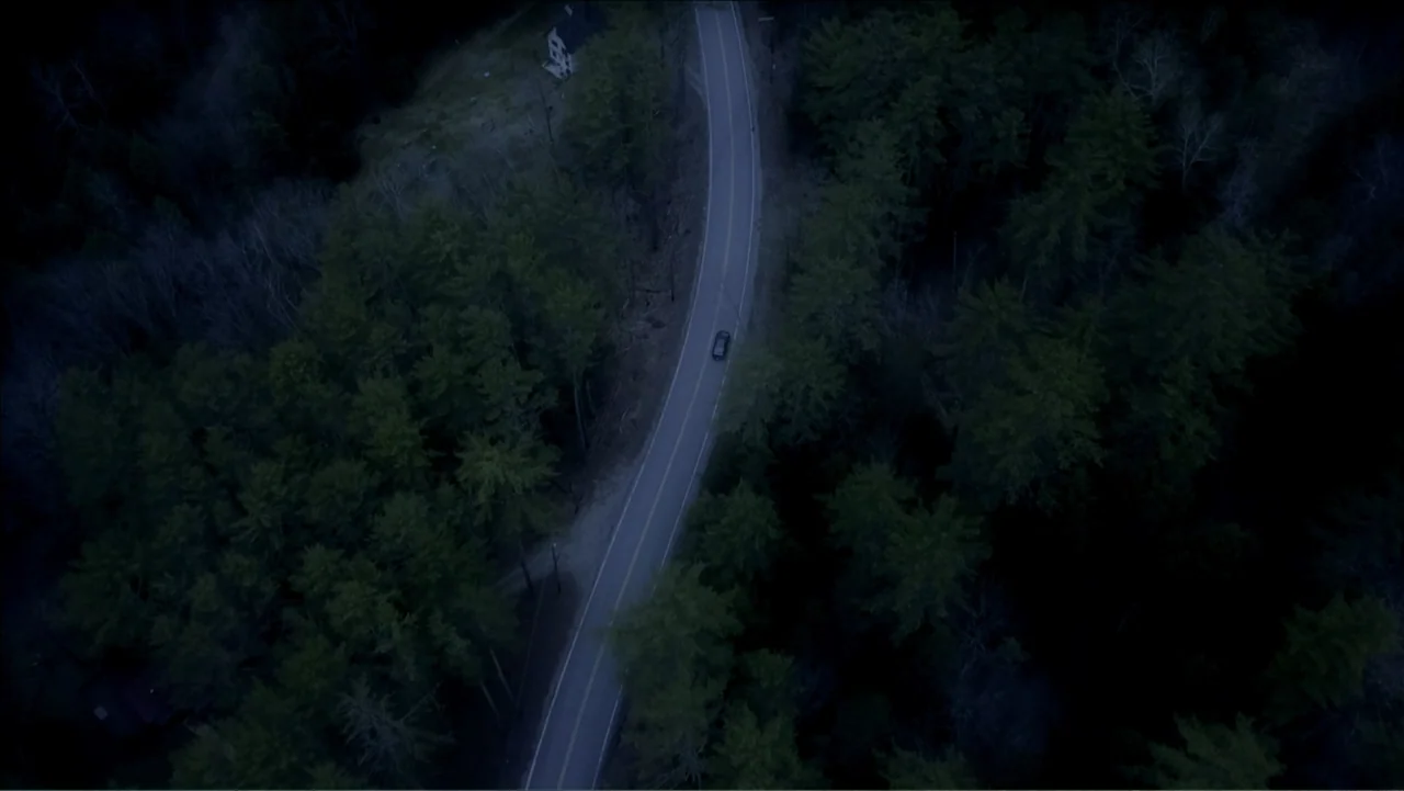 Alien Abduction: Betty and Barney Hill (2022) movie still: establishing — A top-down view shows a narrow asphalt road curving through a dense pine…