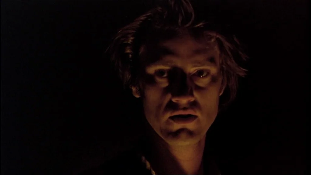 Days Of Heaven (1978) movie still: closeup — The man's face is illuminated from below against a pitch-black background. He stares directly into the…