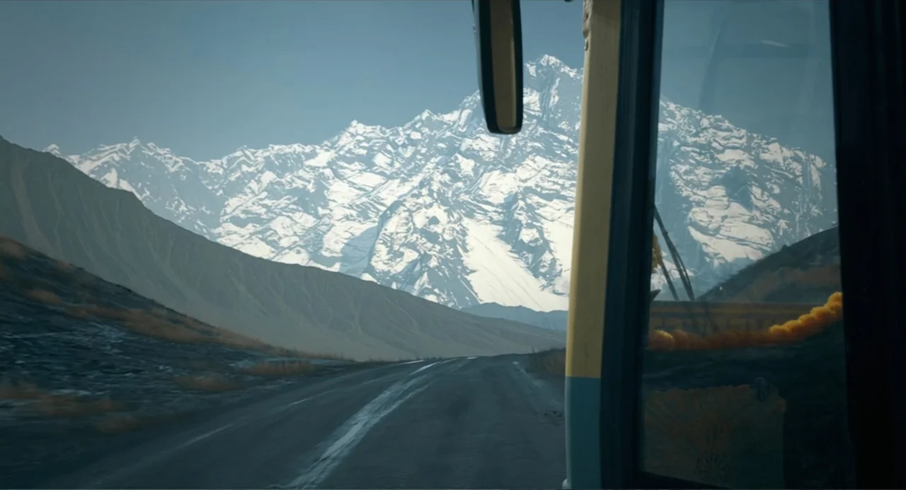 Ice Road: Vengeance (2025) movie still: establishing — A rugged mountain landscape with a long road stretching toward a massive peak. The view is…