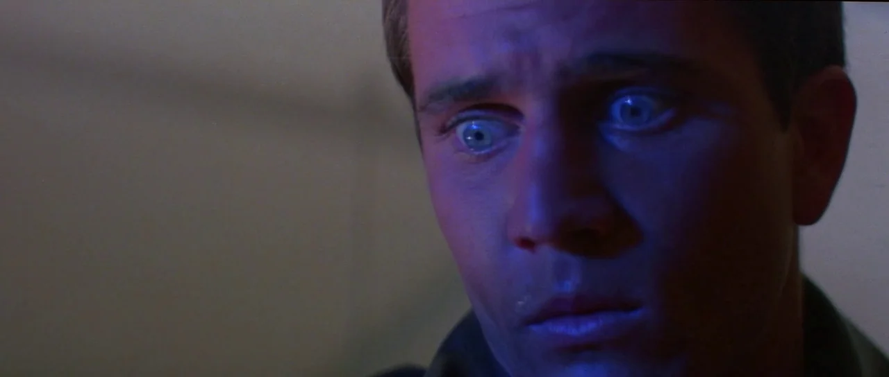 Mad Max (1979) movie still: closeup — The face of a young man is lit in a dark room. He stares wide-eyed at an unseen object off-camera.