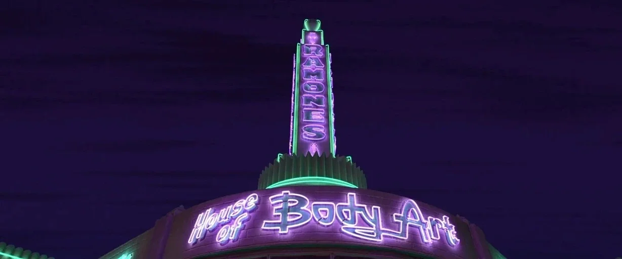 Cars (2006) movie still: establishing — A dark night sky frames the top of a building with glowing neon text. A vertical tower sign reads Ramones…