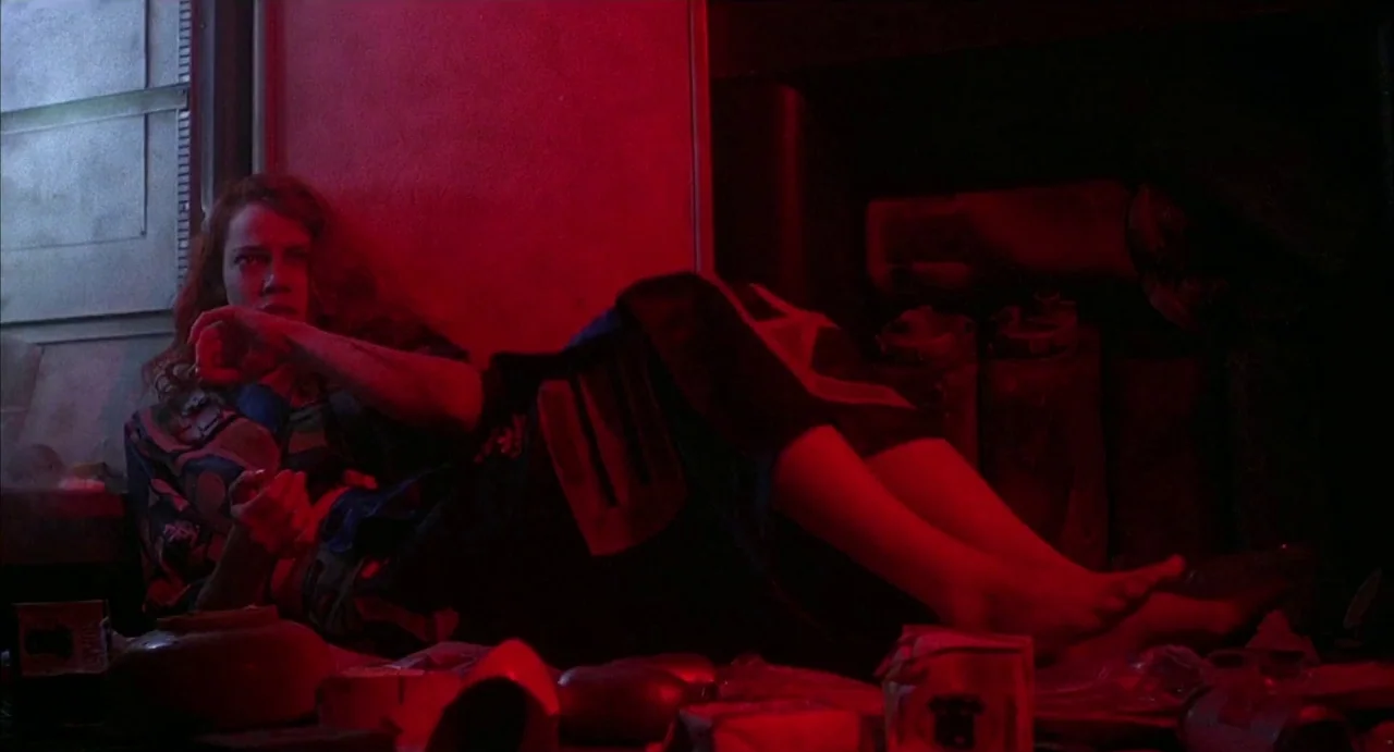 Hardware (1990) movie still: medium — A dark, cluttered interior space is flooded with intense red artificial light. A woman with long wavy hair…