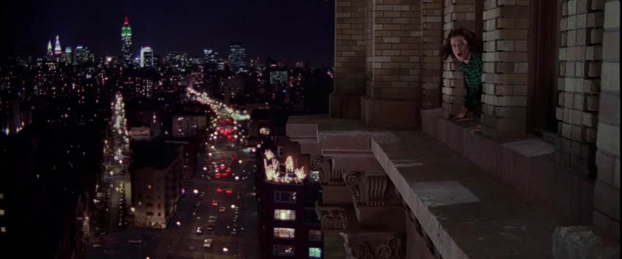 Ghostbusters 2 (1989) movie still: wide — A high-angle view looks down from a brick apartment building ledge over a nighttime city. A woman leans…