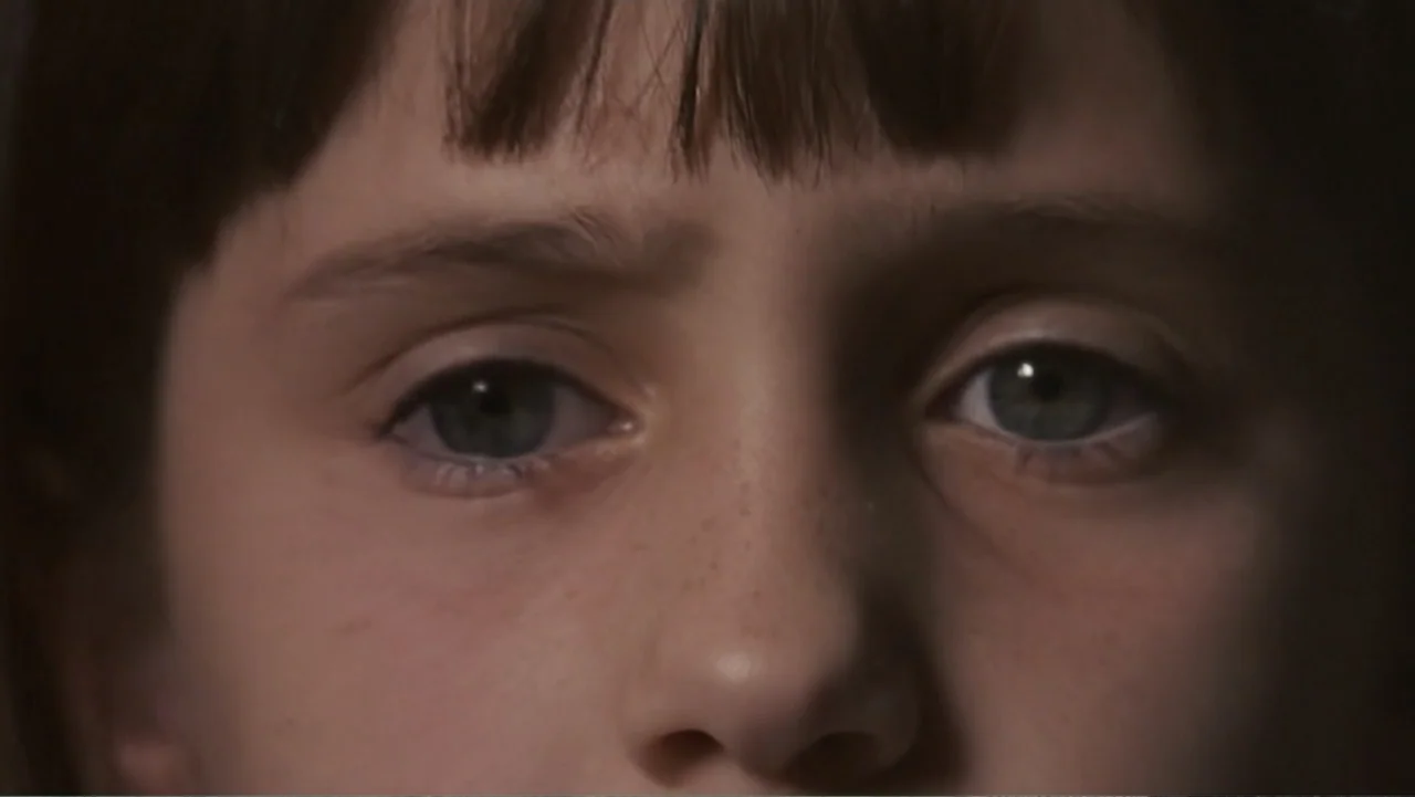 Matilda (1996) movie still: closeup — The face of a young child fills the frame against an out-of-focus background. The child looks directly forward…