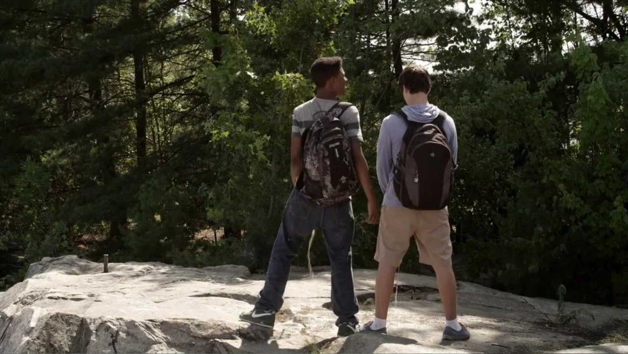 Grown Ups 2 (2013) movie still: fullbody — Two teenagers stand on a large, flat gray rock surrounded by dense pine trees. They both face away from…