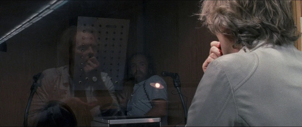Luz (2018) movie still: medium — A recording booth features wood-paneled walls and a glass partition separating two individuals. One man sits in the…